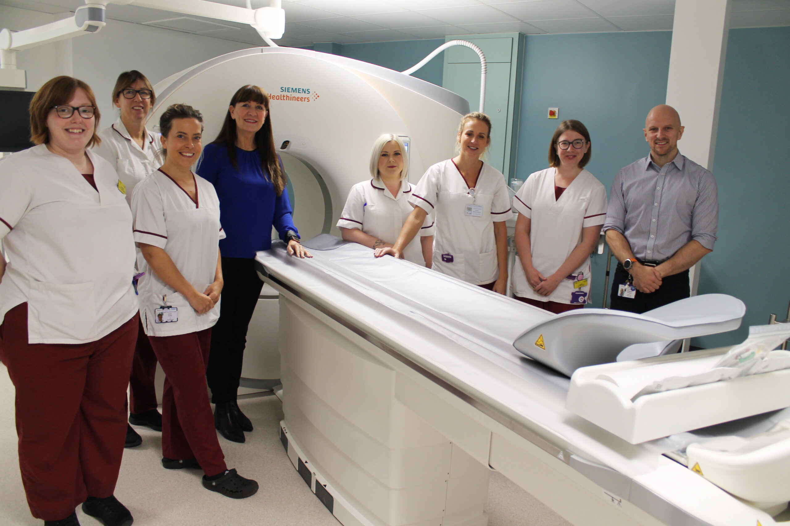 Staff from a radiology department stand in front of a CT scanner