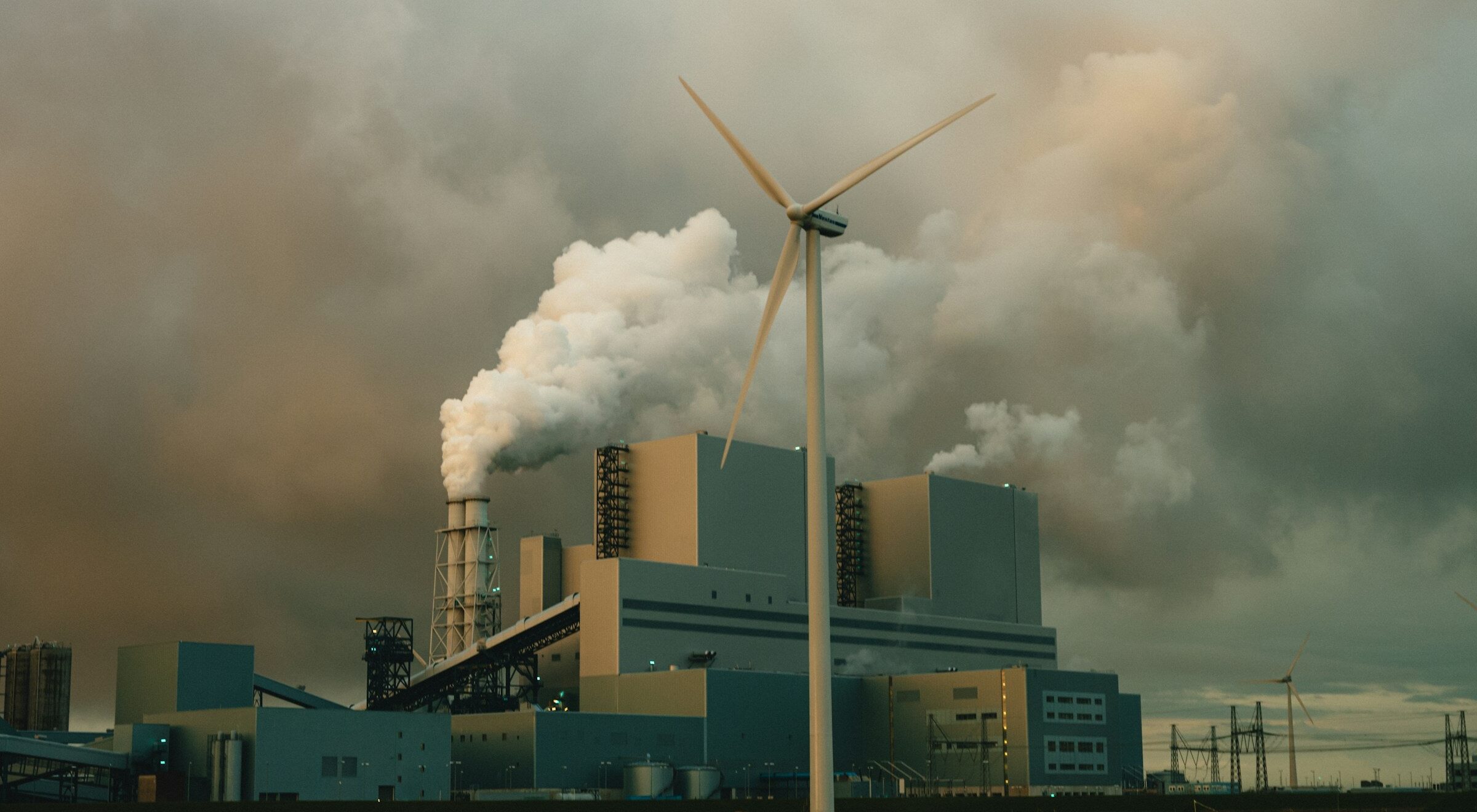 A factory billowing steam, with a wind turbine in front of it